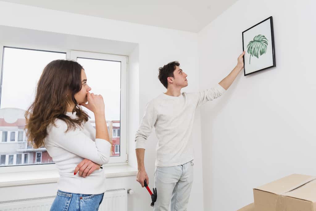 a woman looking at a man who is hanging canvas art